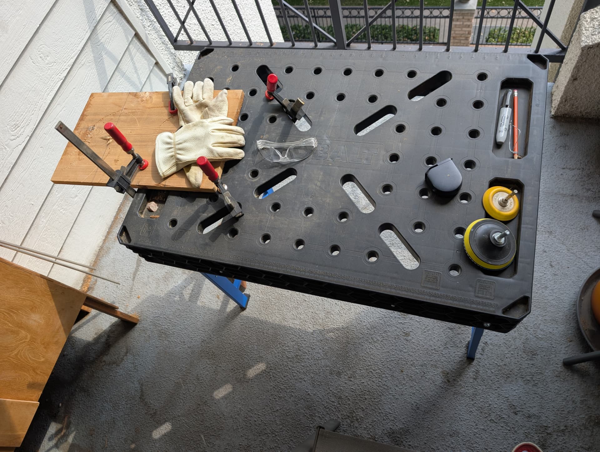 Portable workbench on a front porch with cedar board clamped down, gloves, safety glasses, and sanding discs